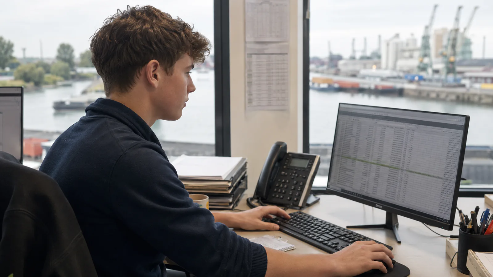 Jovem aprendiz utilizando computador em ambiente profissional ligado ao setor de logística.
